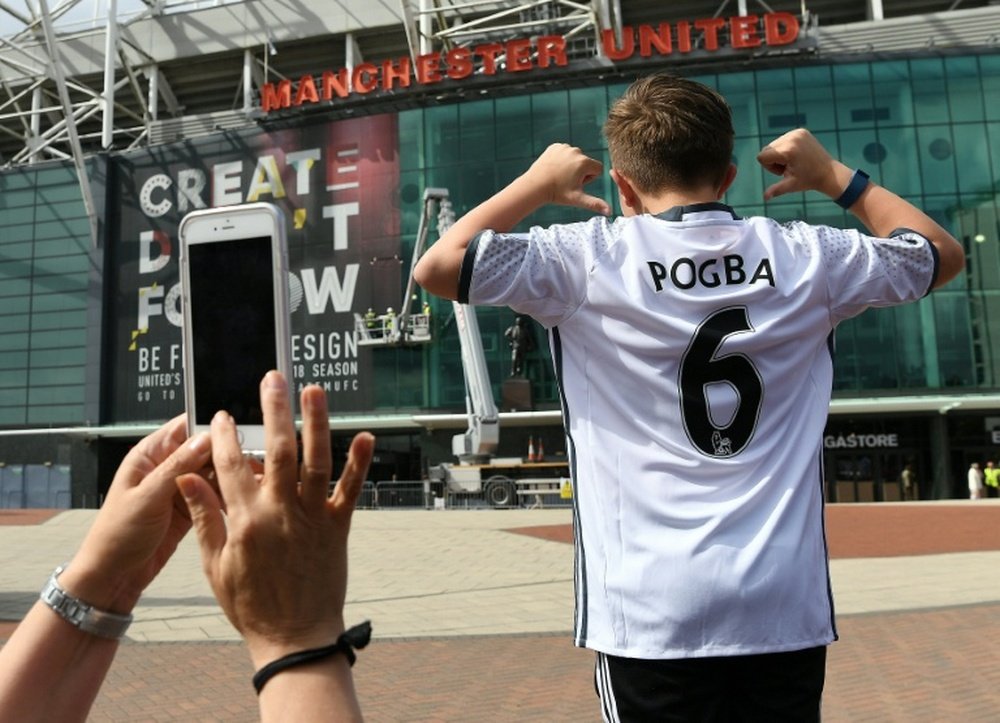 A boy poses for pictures after purchasing a Manchester United shirt with the name and squad number of recent signing French midfielder Paul Pogba outside Old Traford in Manchester on August 9, 2016