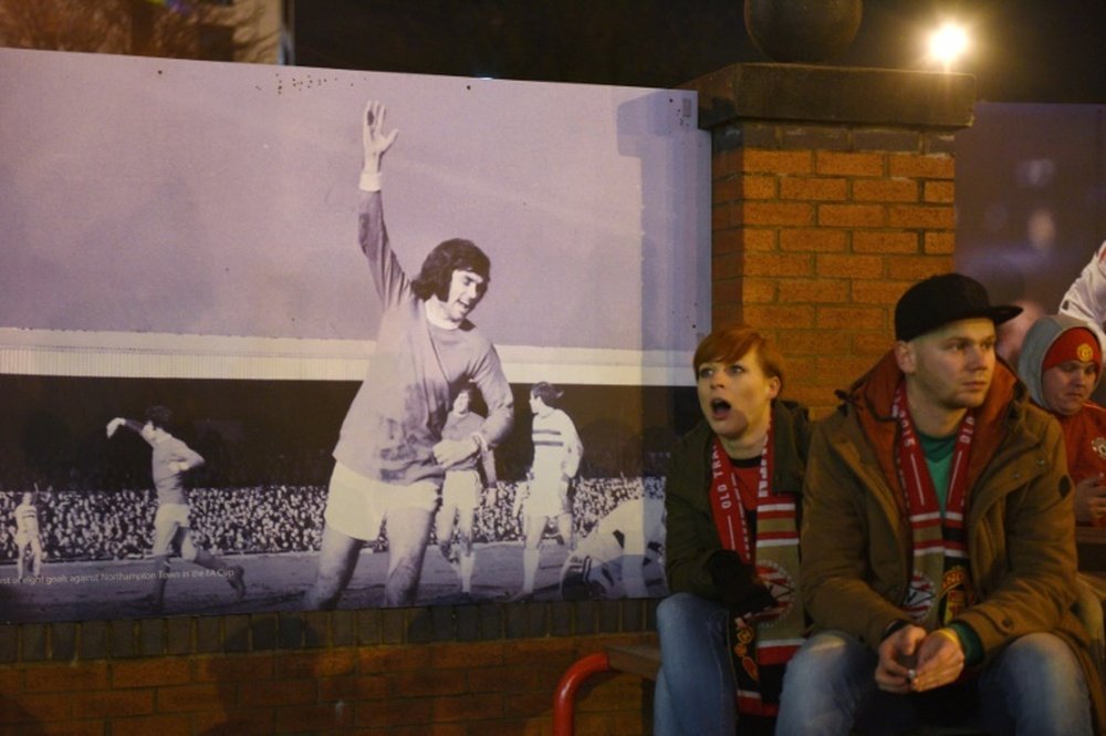 Football fans sit next to a poster of former Manchester United and Northern Ireland footballer George Best on the 10th anniversary of his death, outside Old Trafford Stadium on November 25, 2015