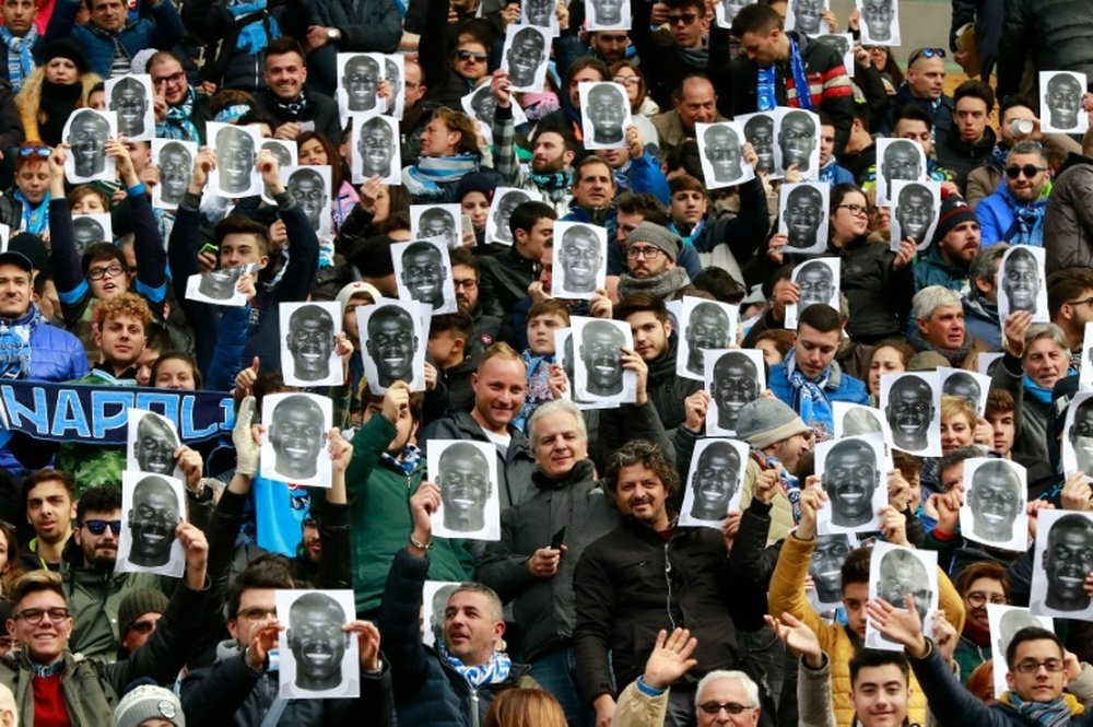 People hold flyers depicting the face of Napolis defender Kalidou Koulibaly before an Italian Serie A football match against Carpi FC on February 7, 2016 at the San Paolo stadium in Naples