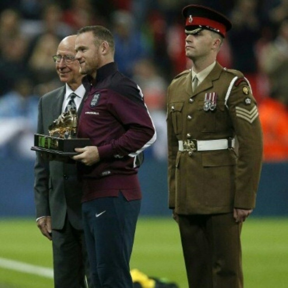 England and Manchester United footballer Wayne Rooney (2nd L) poses for pictures with Sir Bobby Charlton (L) after being presented with a gold plated commemorative boot at Wembley Stadium in north London on October 9, 2015