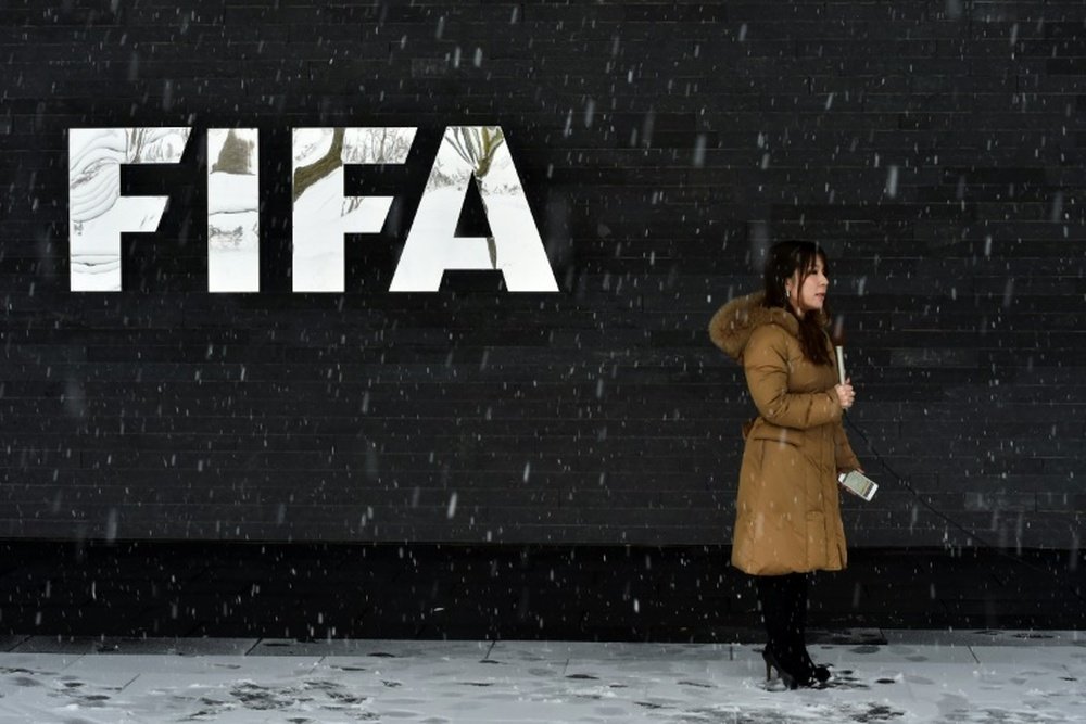 A journalist stands under the snow next to a logo of the FIFA. AFP