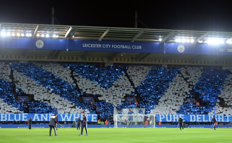 Leicester supporters stand holding coloured card in the club colours. BeSoccer
