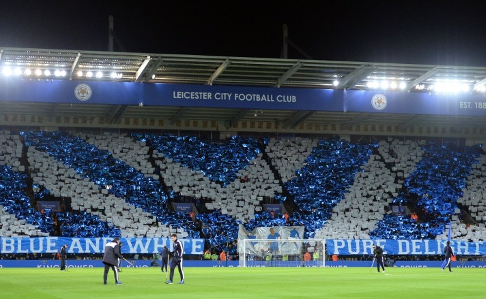 Leicester supporters stand holding coloured card in the club colours. BeSoccer