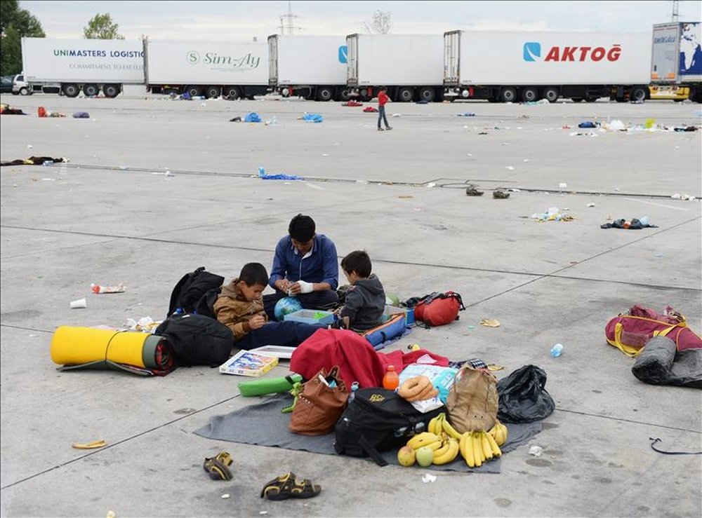 Una familia de refugiados de Oriente Medio permanecen junto a sus pocas pertenencias a la espera de ser trasladados a algún lugar de acogida en la localidad austríaca de Nickelsdorf, tras llegar esta mañana desde Hungría. EFE