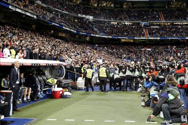 Gran número de fotógrafos y cámaras de video, siguiendo el debut del nuevo técnico francés del Real Madrid, Zinedine Zidane (i), antes del inicio del encuentro correspondiente a la decimonovena jornada de primera división, que disputaron este sábado frente al Deportivo en el estadio Santiago Bernabéu, en Madrid. EFE