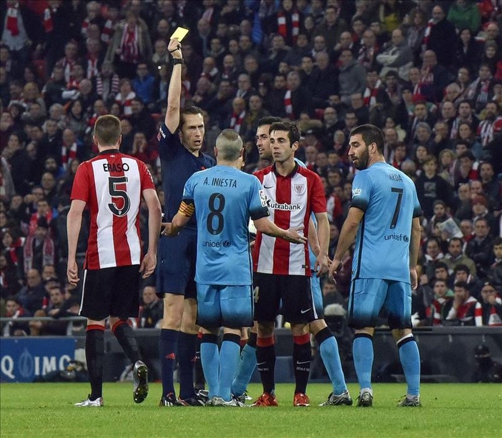 El árbitro saca la tarjeta amarilla al delantero centrocampista del FC Barcelona Andrés Iniesta, durante el partido de ida de cuartos de final de la Copa del Rey que se juega hoy en San Mamés. EFE