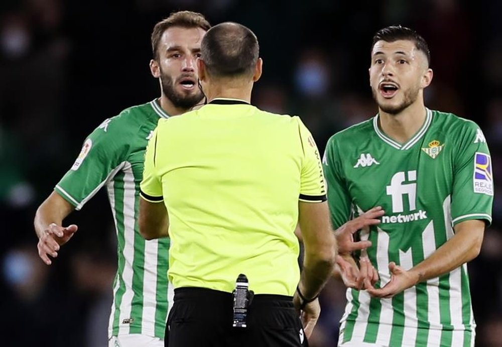 Los jugadores del Betis, el argentino Guido Rodríguez (d) y Alex Moreno protestan al colegiado Mateu Lahoz la tarjeta roja que ha mostrado al centrocampista argentino durante el encuentro correspondiente a la decimotercera jornada de primera división que disputaron frente al Sevilla en el estadio Benito Villamarín de la capital andaluza. EFE/ José Manuel Vidal.