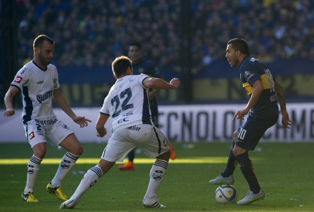 Carlos Tevez (R) vies for the ball with Adrian Calello (C) and defender Mariano Uglessich during their Argentina First Division football match in Buenos Aires, Argentina, on July 18, 2015.