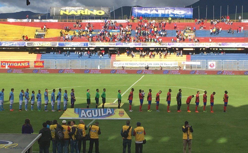 Los onces iniciales del Deportivo Pasto y el Atlético Junior escuchan el himno antes del encuentro que le enfrentó en la quinta fecha del Clausura 2016. Twitter/DeporPasto
